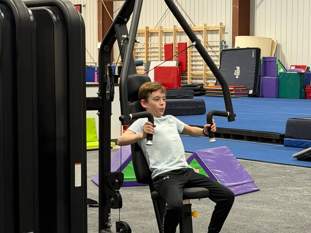A child working on a seated machine in the youth fitness room