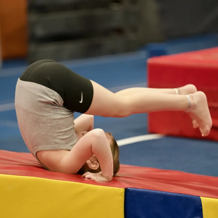 A young gymnast holding a headstand on the red mat