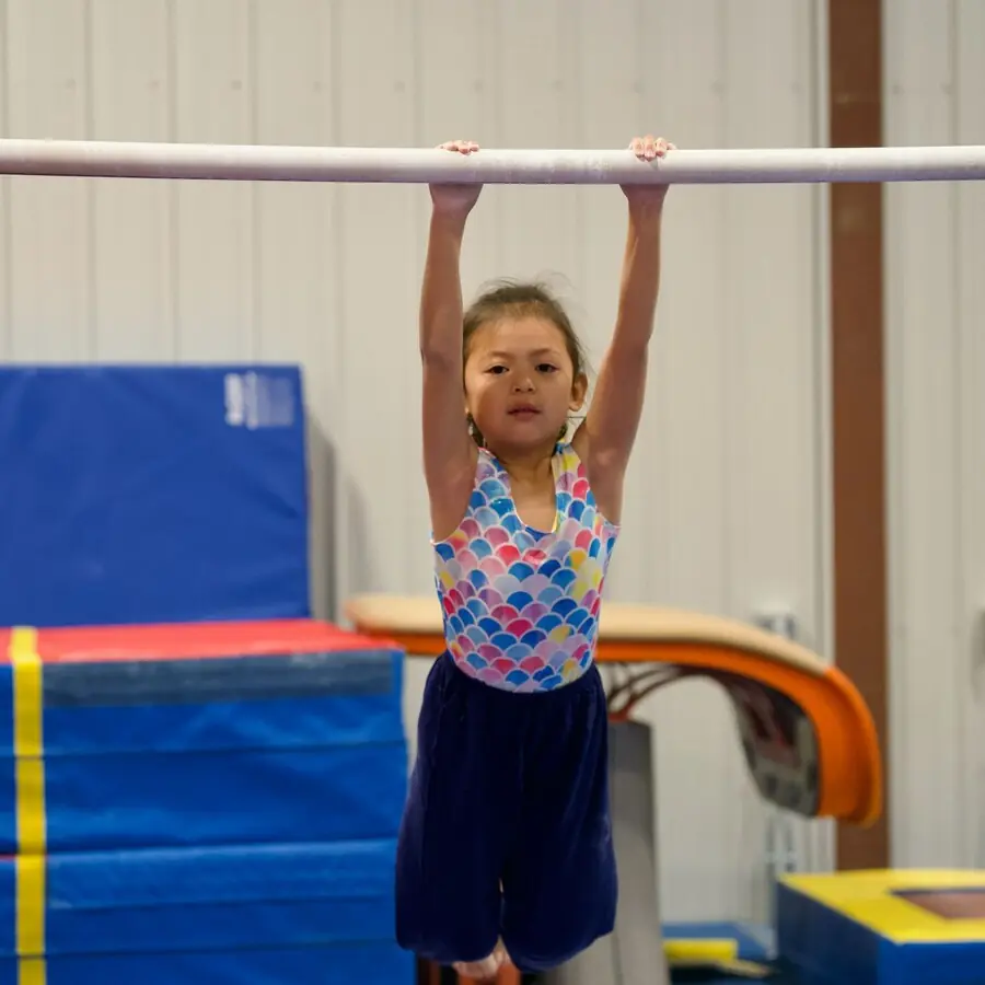 A child hanging from the low bar over the foam pit
